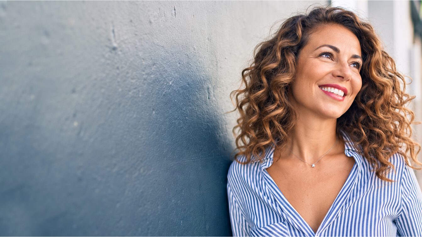 Smiling woman with curly hair leaning against a wall